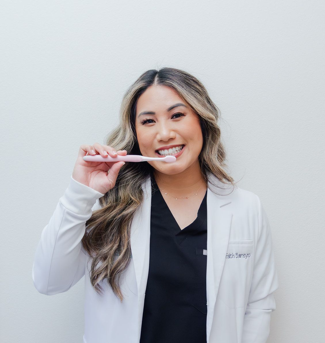 Woman in lab coat brushes her teeth, smiling.