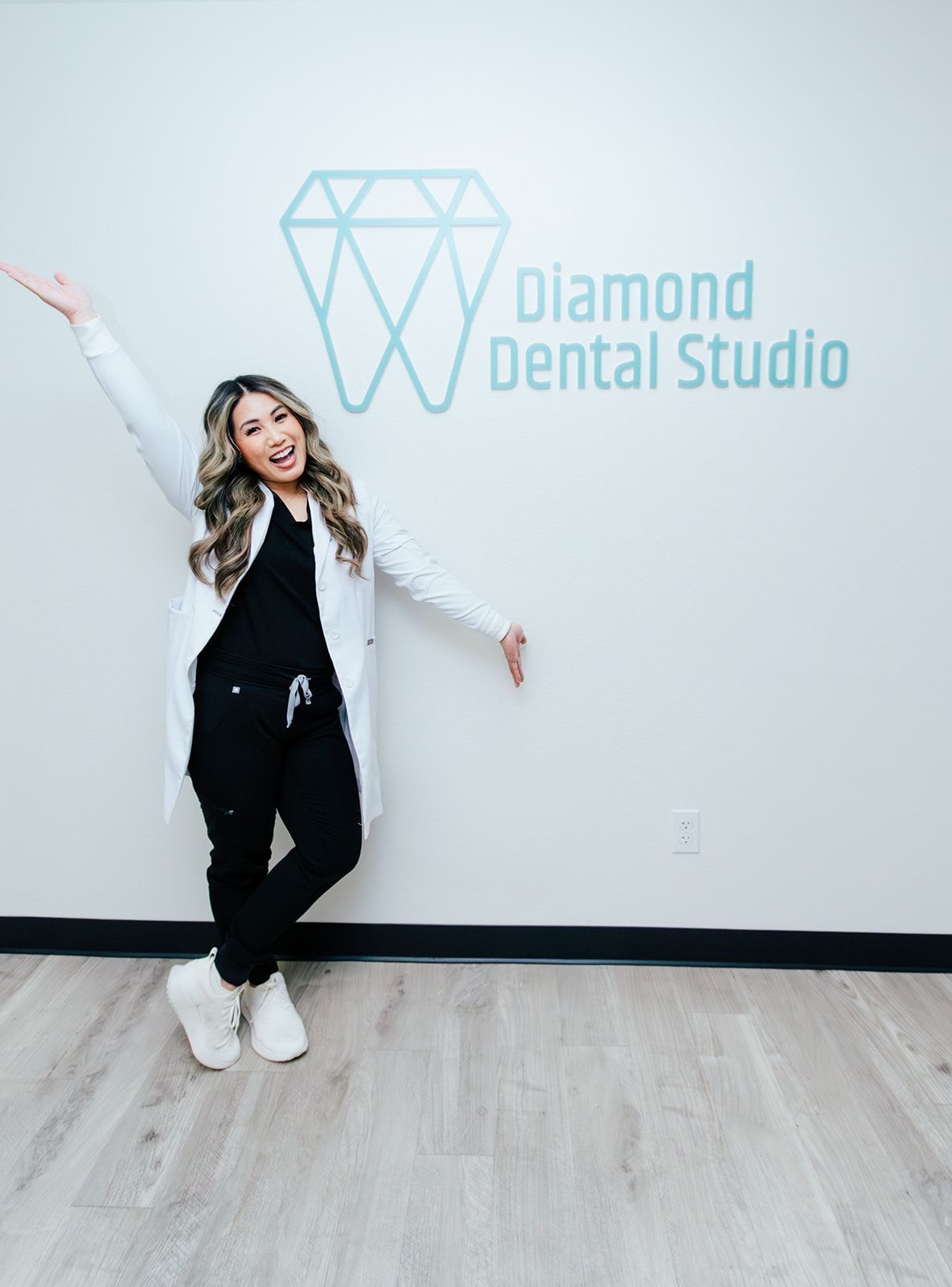 Dentist in black scrubs and white coat smiles, arm raised, by Diamond Dental Studio logo.