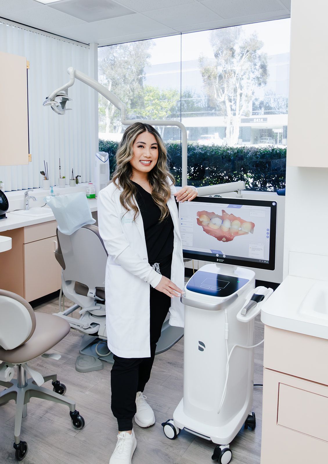 Dentist in white coat smiles, holding a device in a modern dental office.