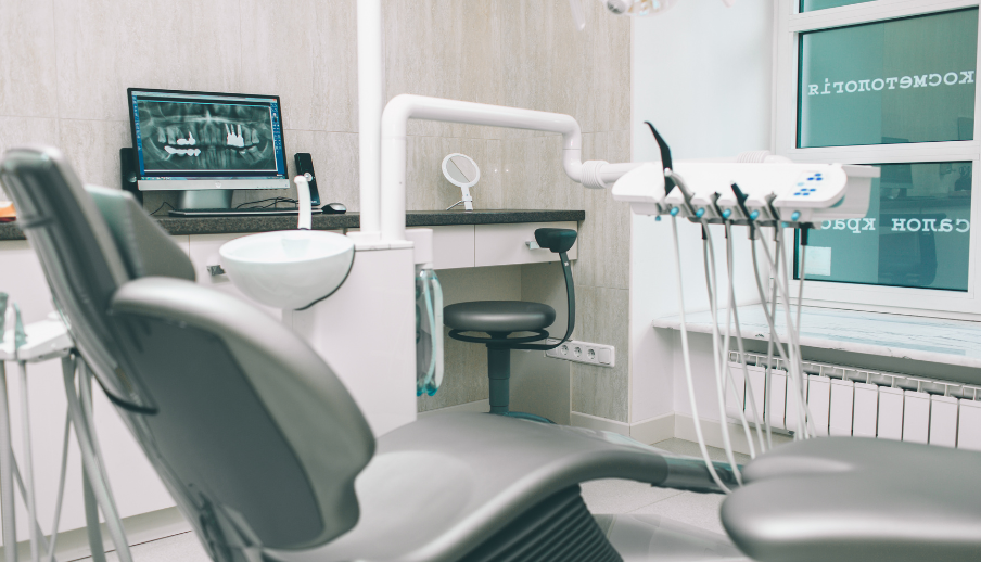 Dental office with chair, instruments, and x-ray monitor. Gray and white interior.