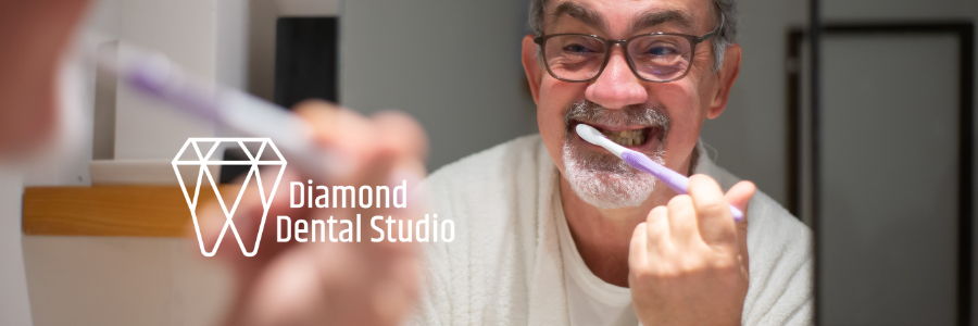 Man brushing his teeth in bathroom, reflected in mirror. Diamond Dental Studio logo in the bottom left.