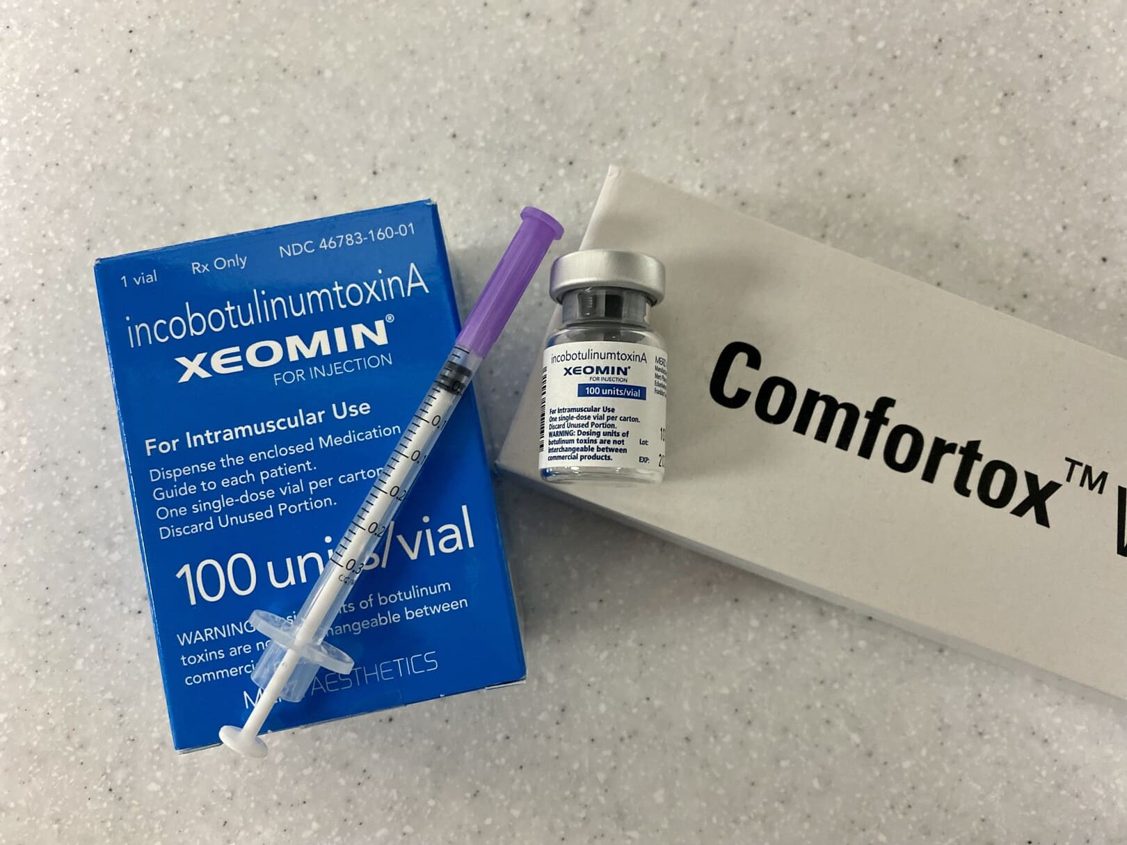 Box and vial of Xeomin, syringe, and a box labeled Comfortox on a light surface.