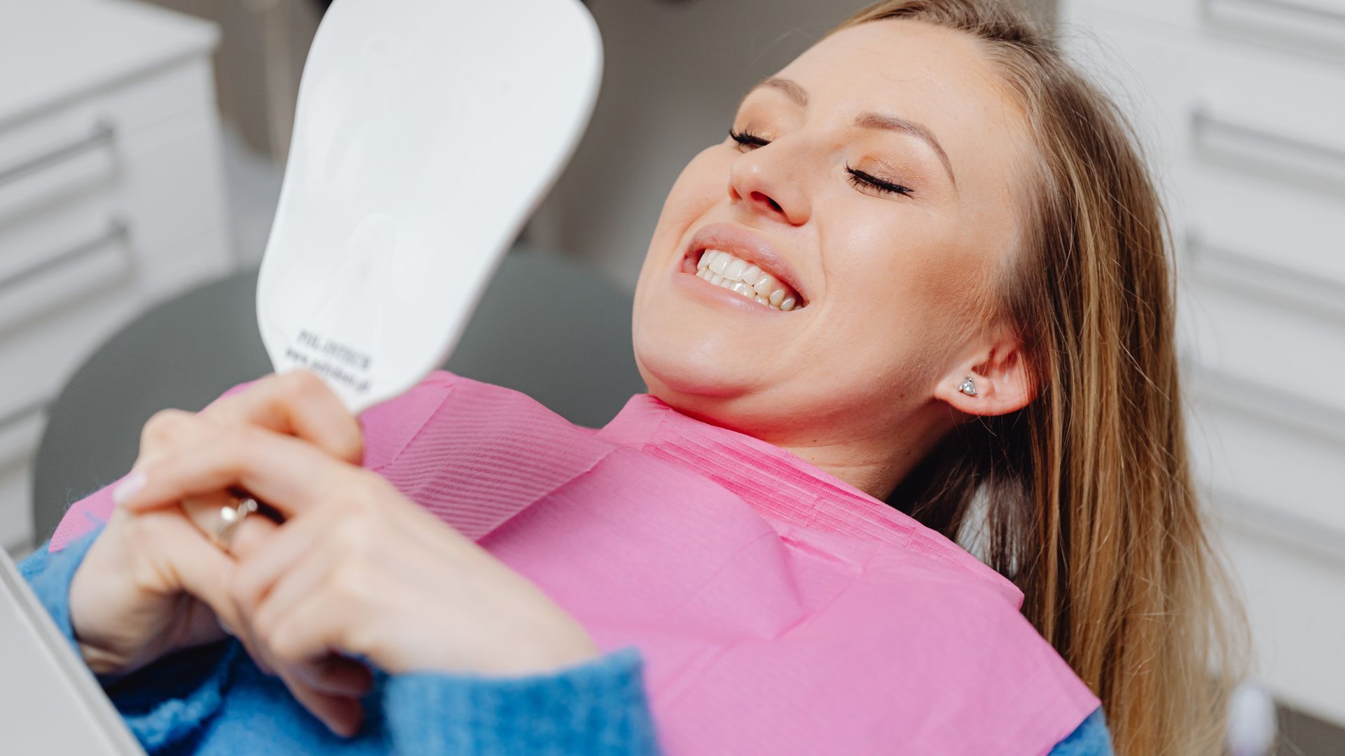 Dental patient in pink bib smiling with a dental mirror during an exam