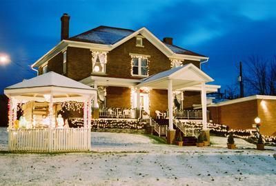 Snowy two-story brick house with porch, gazebo, and lawn under a twilight sky.