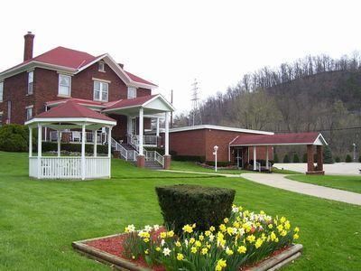 A red brick building with a gazebo and a driveway with a small garden in the foreground.