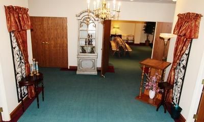 Hallway with teal carpet, wood doors, ornate chandelier, and display cabinet.