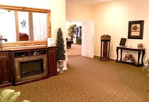A room with a fireplace, mirror, and a doorway leading to a hallway with plants.