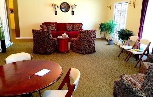 Waiting room with burgundy sofa, patterned armchairs, round table, and folding chairs.