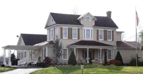 Two-story beige house with a porch and carport, brown shutters, a flagpole, and a green lawn.