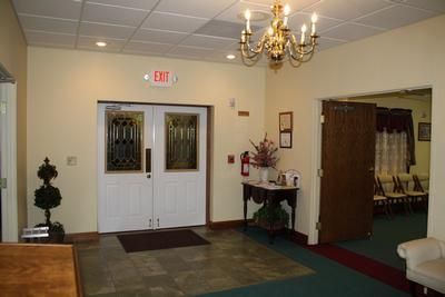 Entrance to a building with double doors, exit sign, chandelier, and a table with flowers.