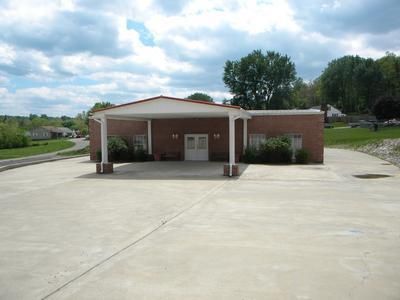 Brick building with white pillars and canopy. Large concrete parking area. Overcast sky.