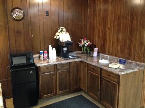 Coffee station with microwave, mini-fridge, coffee maker, flowers, cups, and snacks set against wood paneling.