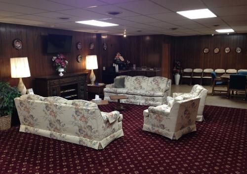 Cozy waiting room with floral couches, lamps, and a TV. Wooden paneling and red carpet.