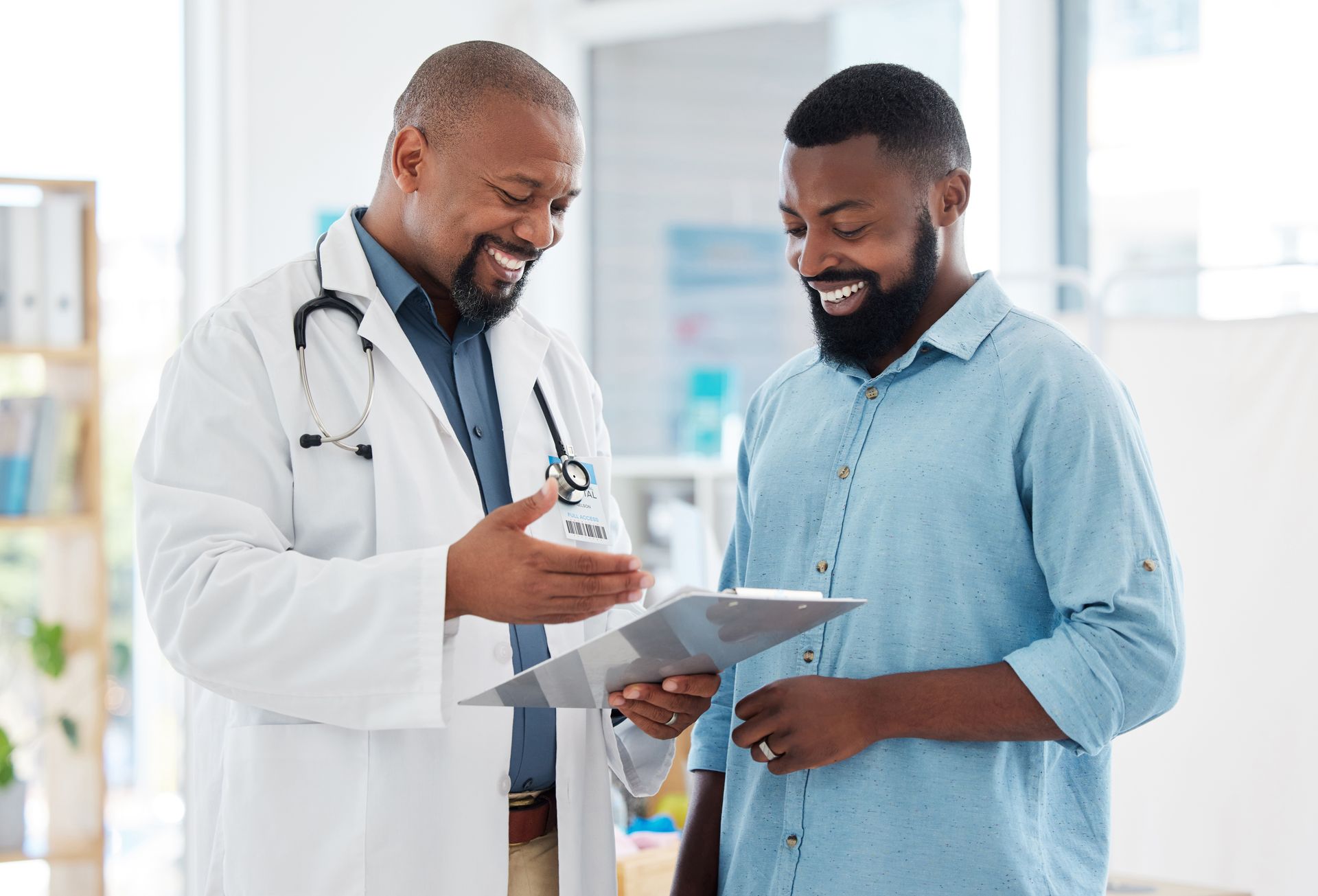 Black woman smiles at doctor, hand on her chest. Doctor has hand on her shoulder. Indoors.