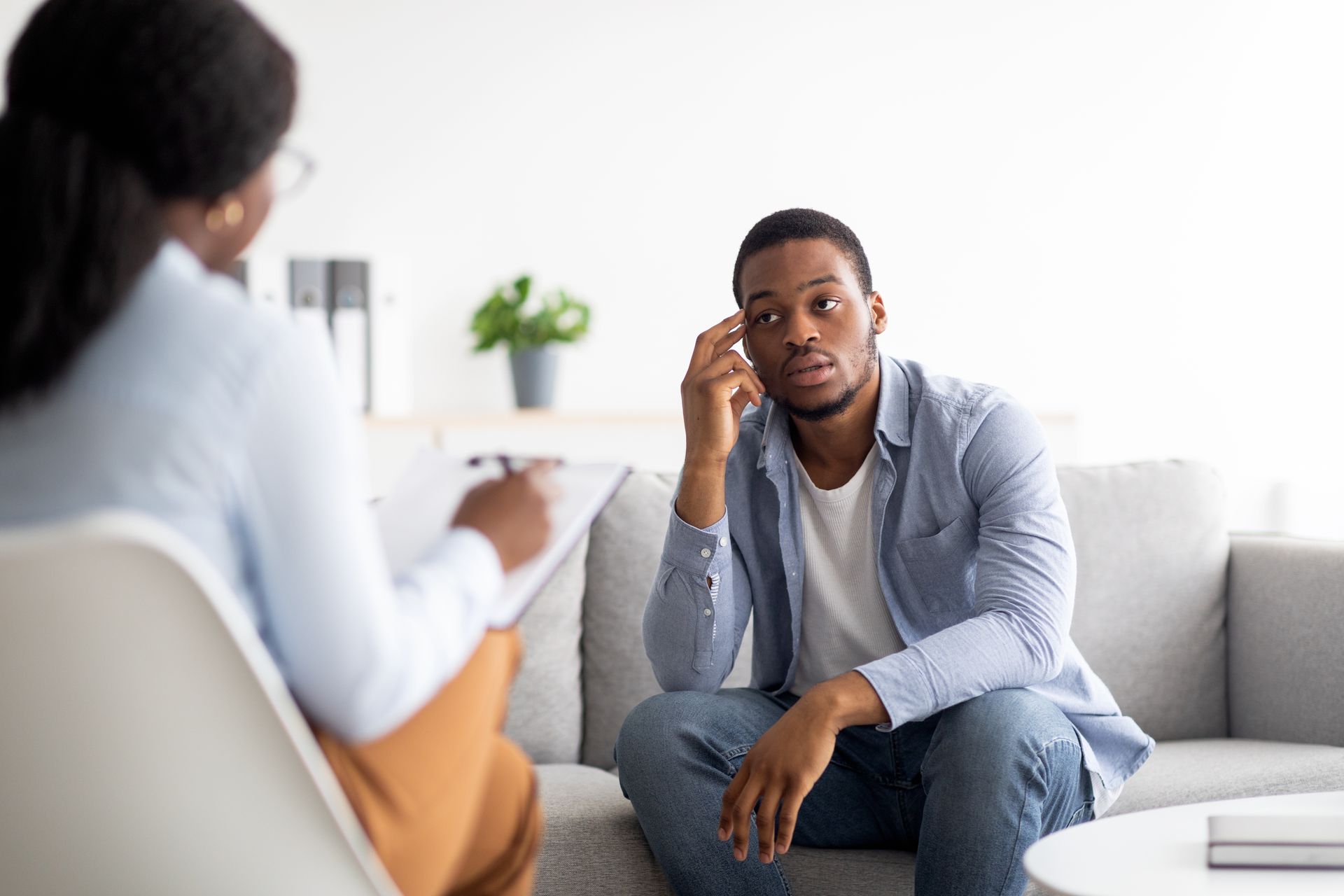 A Black man in therapy, looking pensive, talking with a Black therapist.
