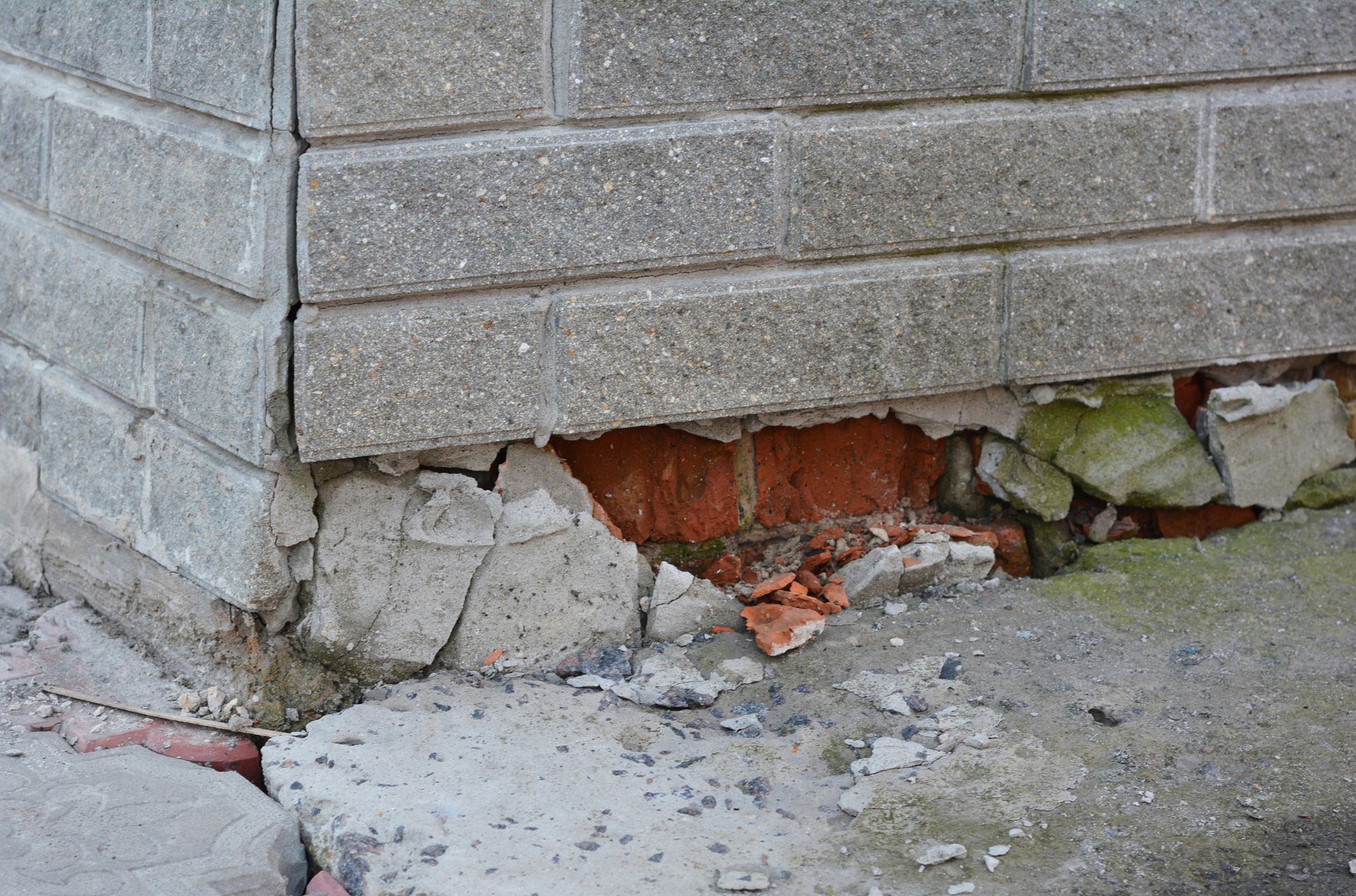 Damaged brick foundation corner with crumbling concrete and exposed red brick.