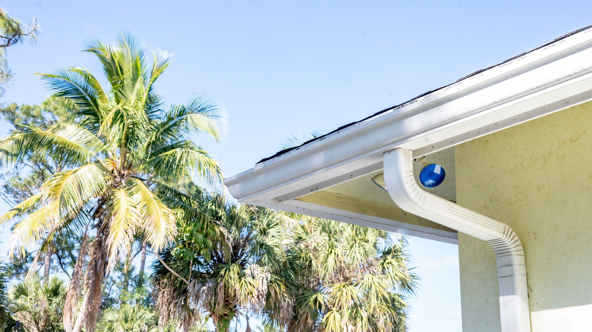 White gutters on a yellow house with a palm tree, clear blue sky. White gutters on a yellow house with a palm tree, clear blue sky.