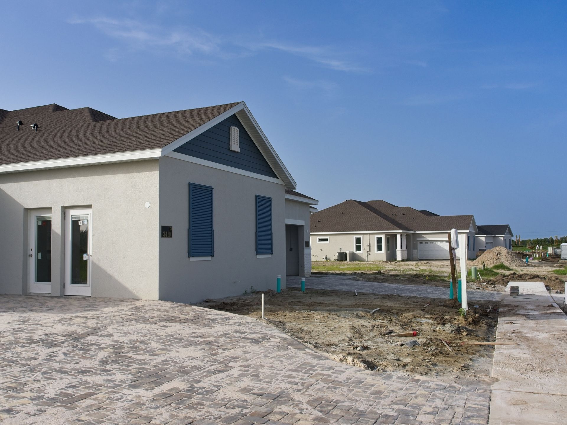 New homes under construction, stucco exterior, blue shutters, clear sky.