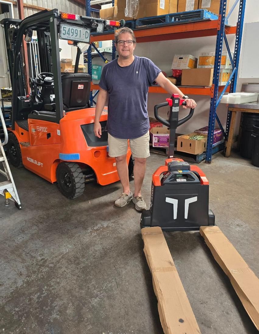 Man in Warehouse Stands by Orange Forklift — A1 Forklifts In Port Macquarie, NSW