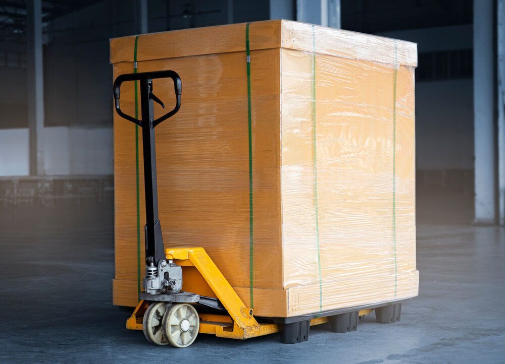 Yellow Pallet Jack Lifting a Large, Wood Crate Wrapped — A1 Forklifts In Macksville, NSW