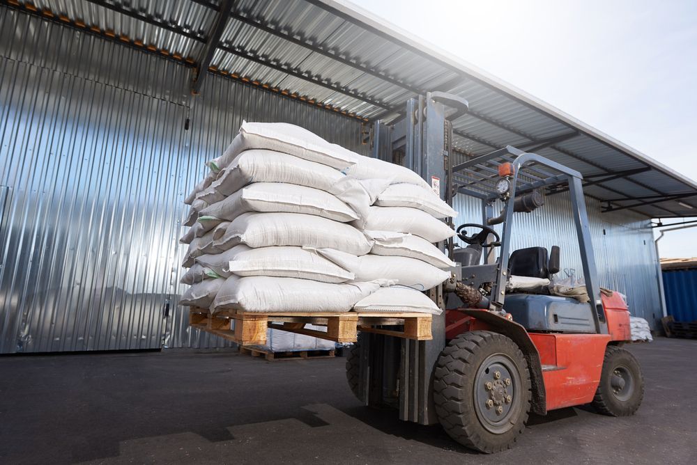 Red Forklift Carrying a Pallet Stacked With White Bags in a Warehouse — A1 Forklifts In Forster, NSW