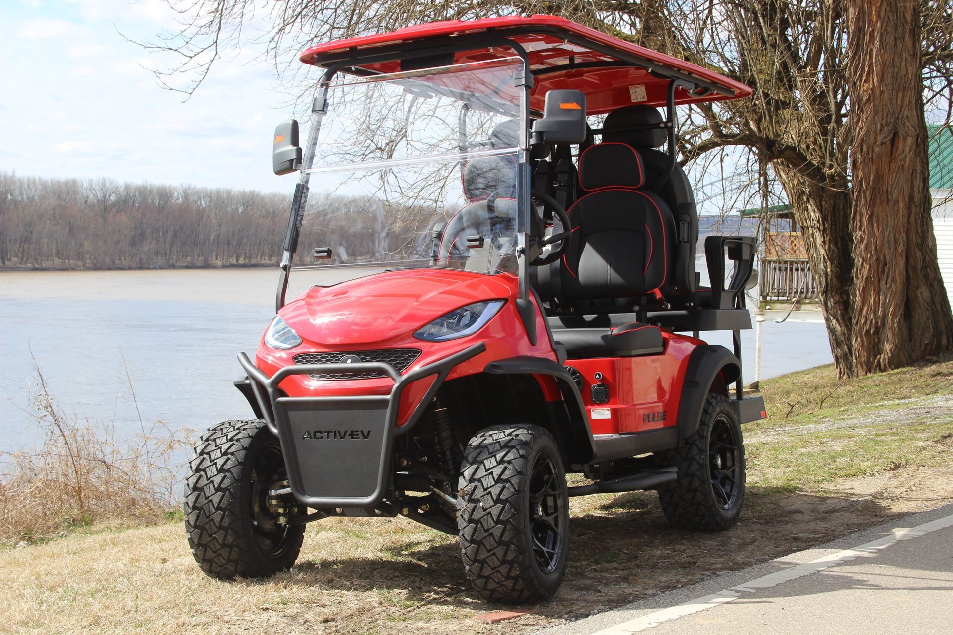 A red golf cart is parked on the side of the road next to a lake.
