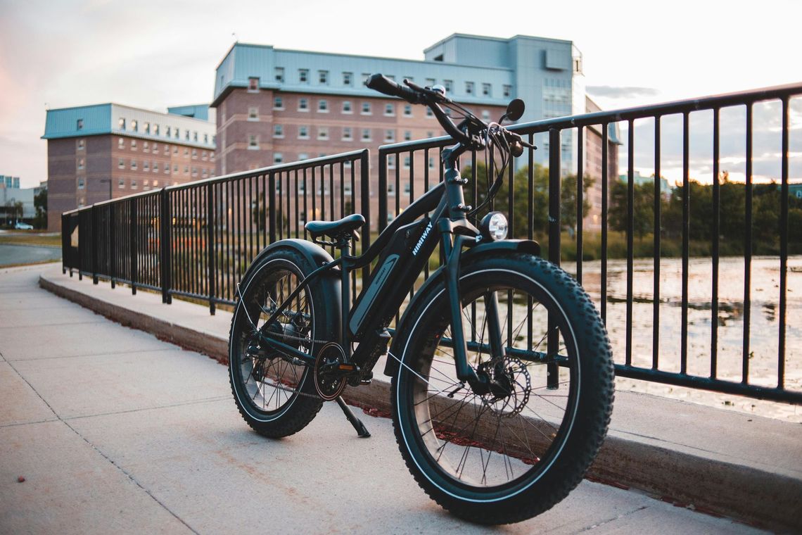 A black bicycle is parked on a sidewalk next to a railing.