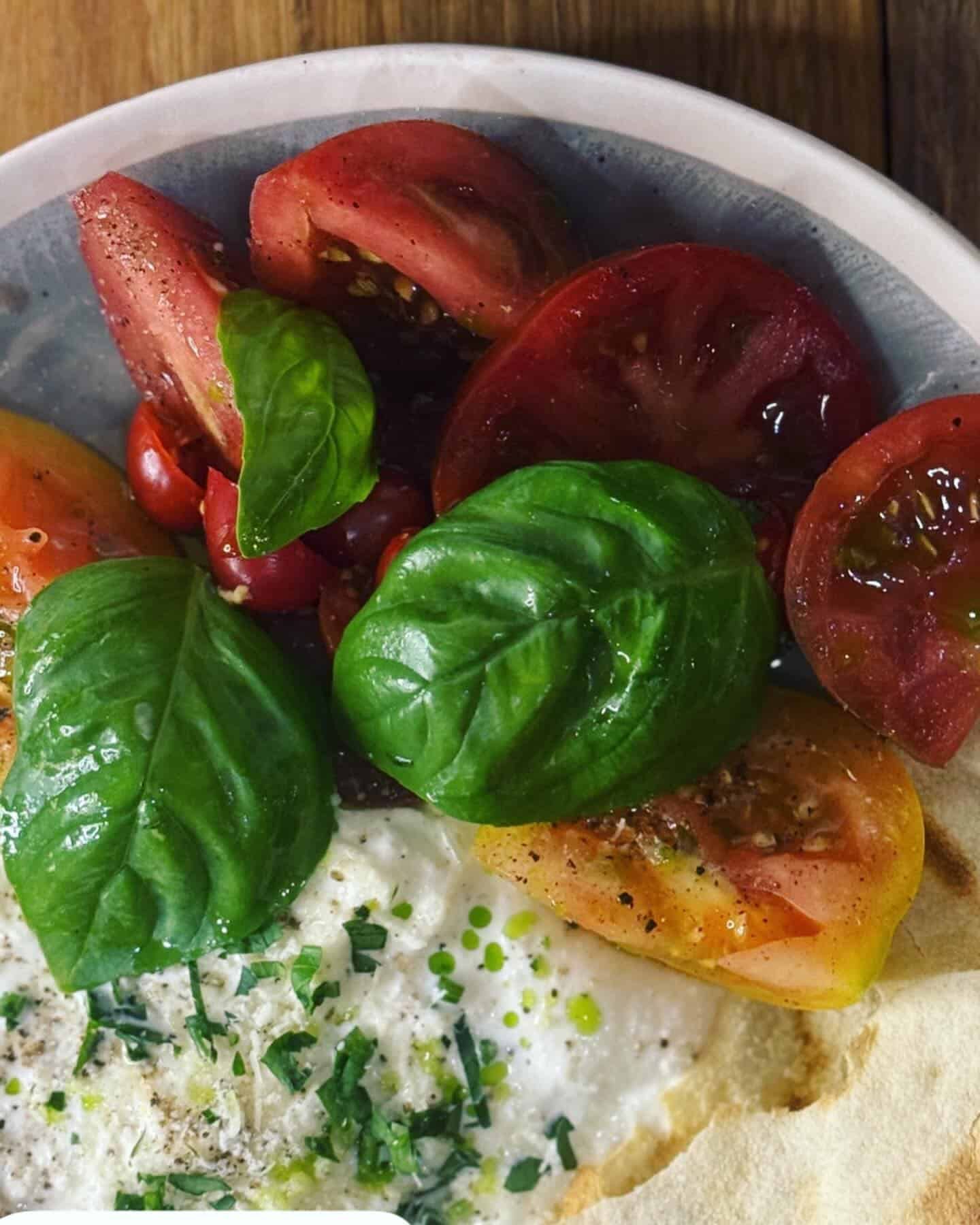 A Close Up of a Plate of Food With Tomatoes and Basil on a Table — Onesta Cucina in Bowral, NSW