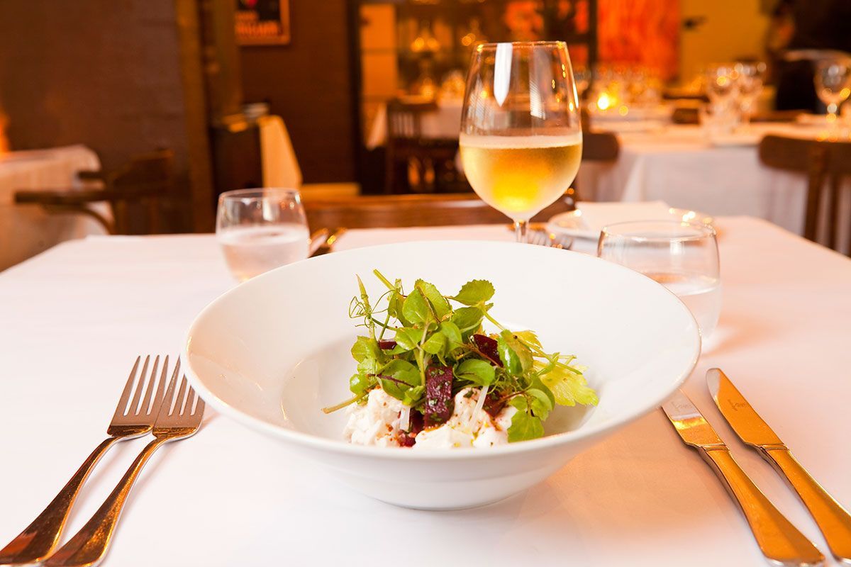 A Bowl of Salad is on a Table Next to a Glass of Wine — Onesta Cucina in Bowral, NSW
