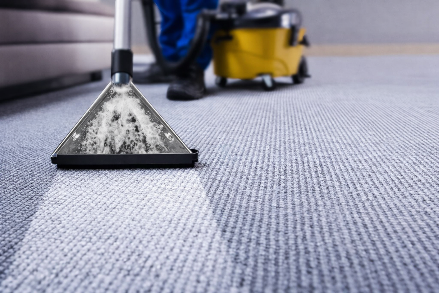 A professional cleaner using a yellow extraction machine to deep clean a gray carpet.