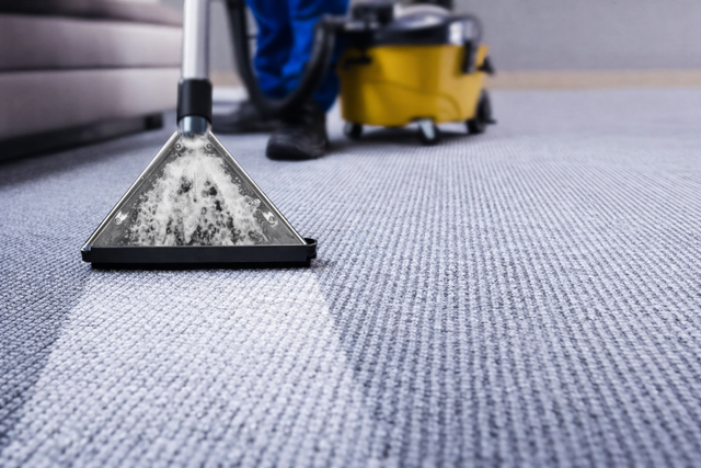 A professional cleaner using a yellow extraction machine to deep clean a gray carpet.