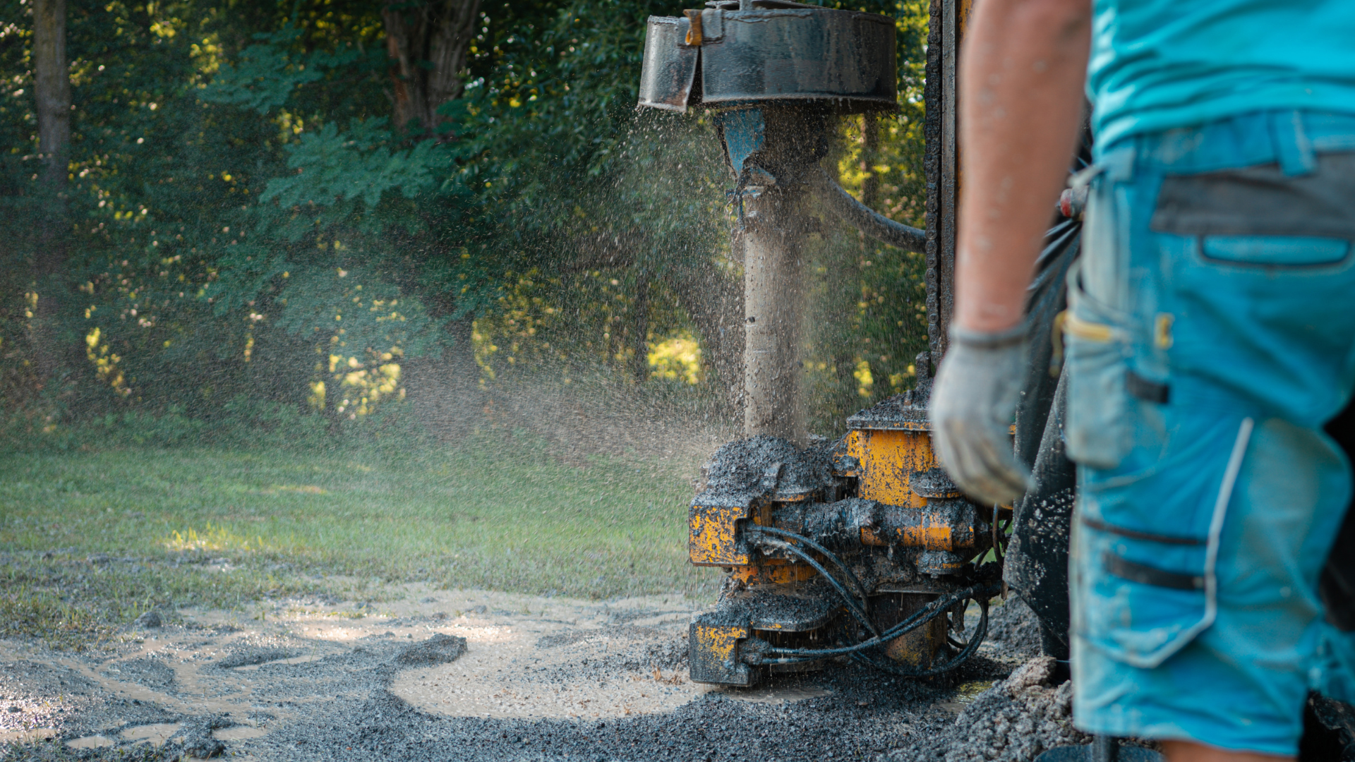 A man is standing next to a machine that is drilling a hole in the ground.