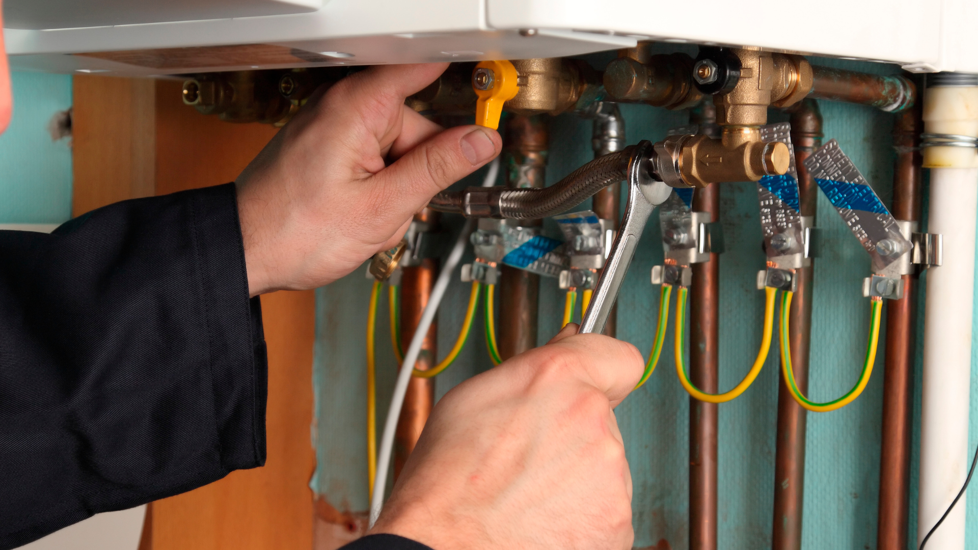 A man is fixing a boiler with a wrench.
