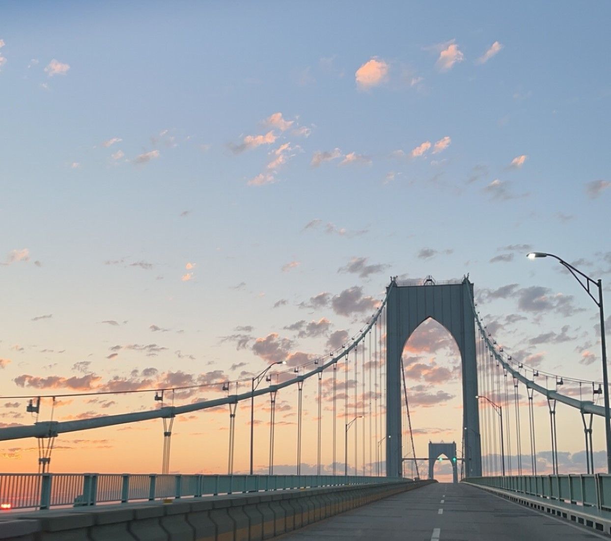 The Newport Pell Bridge during sunset with a clear view of the iconic arch and suspension cables against a pastel sky.