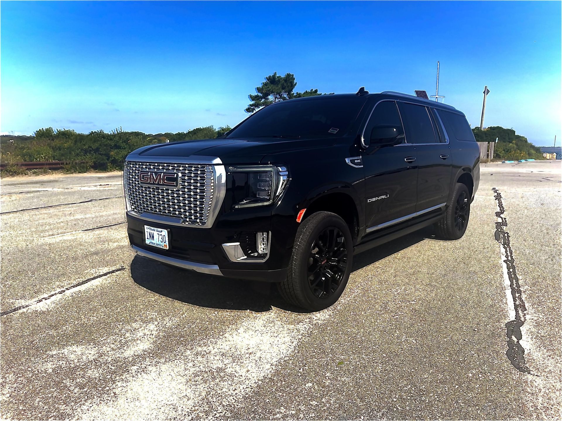 A black GMC Yukon SUV parked on a paved lot under a clear blue sky.