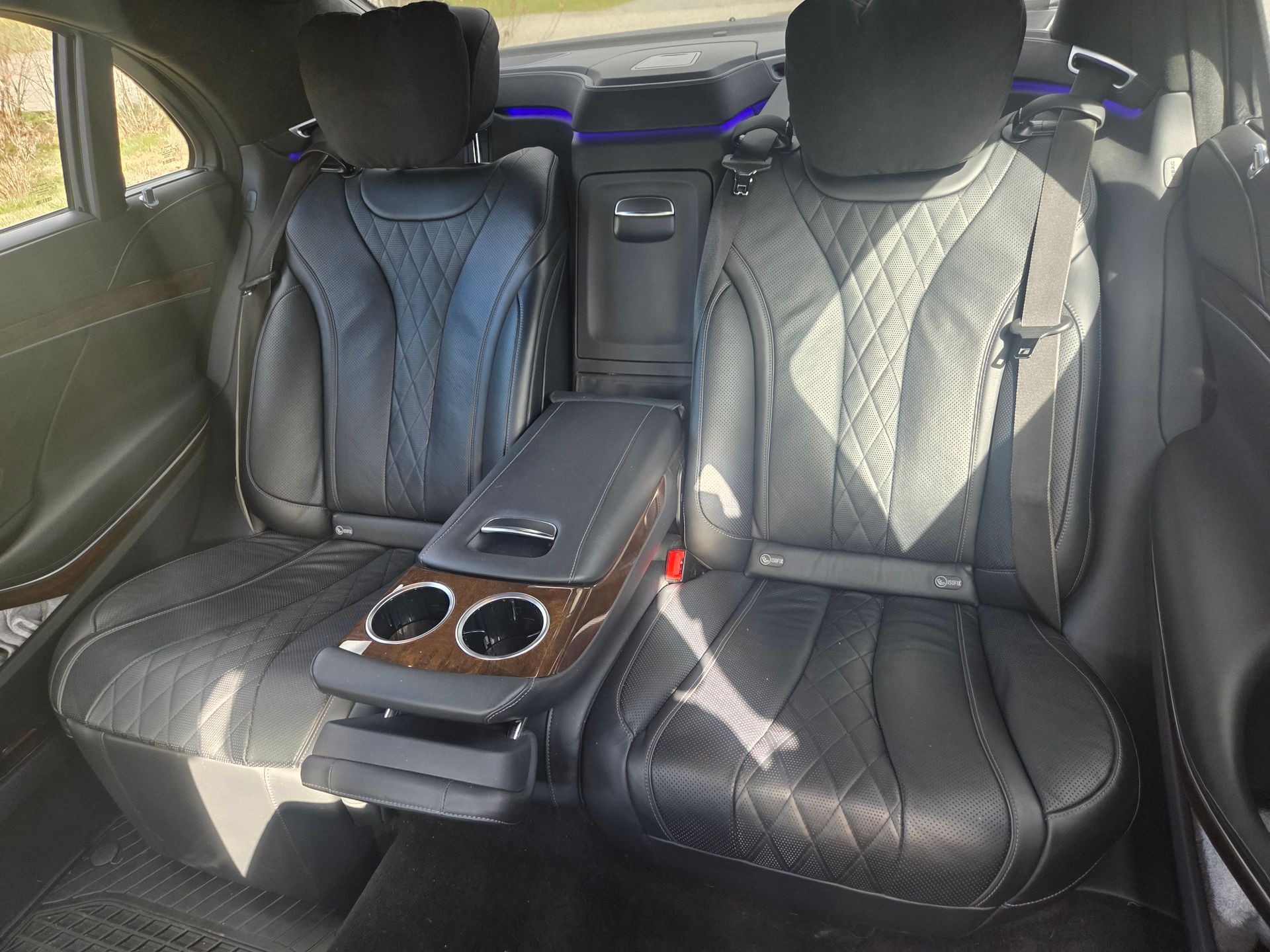 Black leather car seats with diamond-stitched patterns, featuring a central wood-grain armrest and two cup holders.