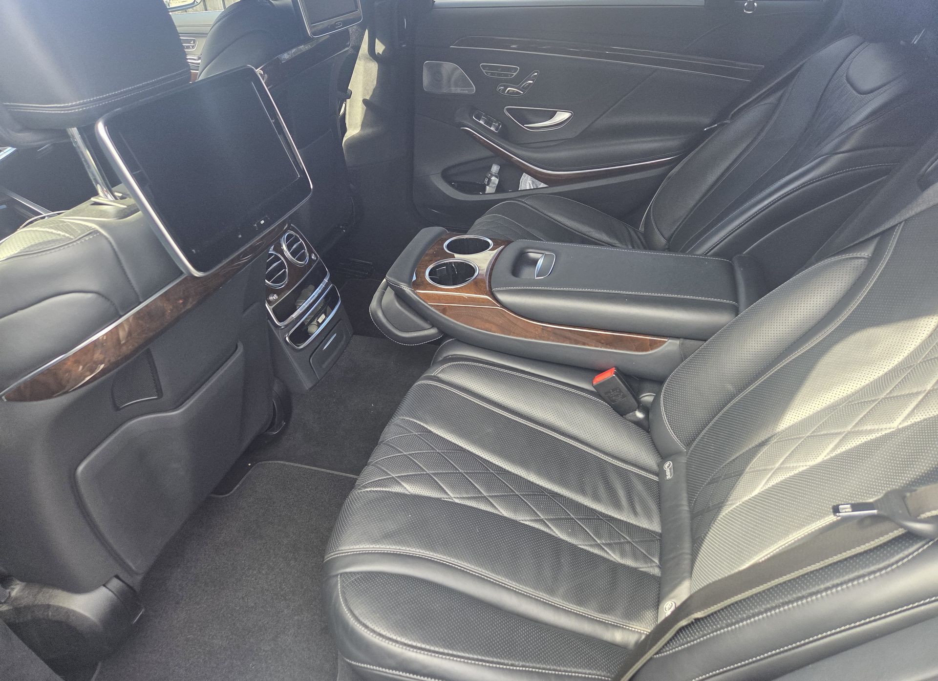 The interior of a luxury car's backseat with black quilted leather seats, wood trim, and an integrated headrest screen.