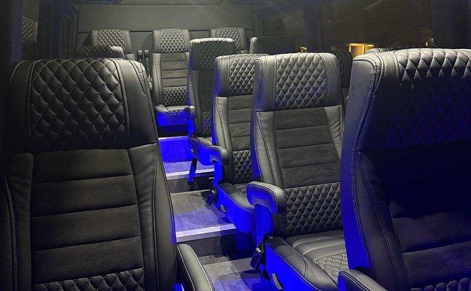 Interior of a vehicle featuring rows of black, diamond-stitched luxury leather captain's chairs with blue ambient lighting.