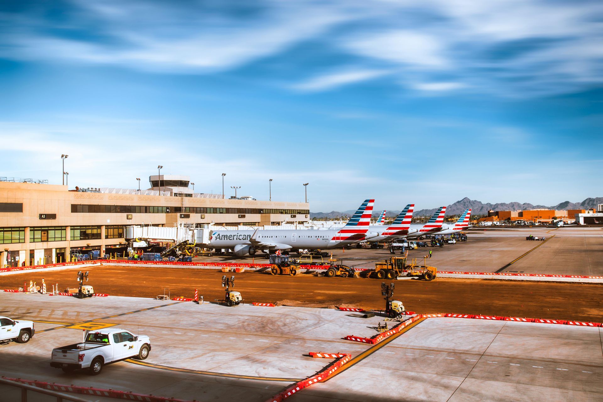 Multiple American Airlines planes parked at an airport terminal under a clear blue sky.
