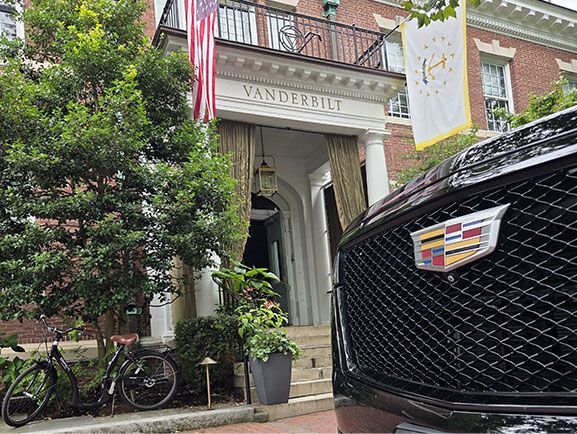 A black Cadillac grill in the foreground, with a historic brick Vanderbilt building, a US flag, and a bicycle nearby.