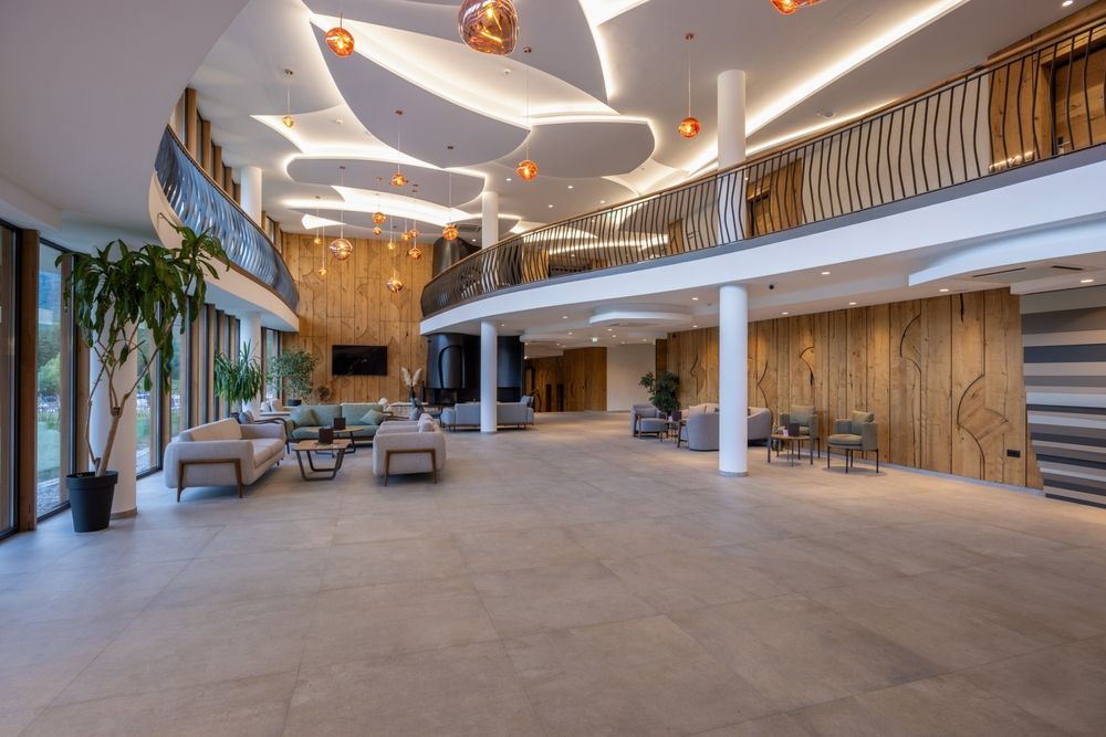 A spacious hotel lobby with neutral-toned stone floors, wood-paneled walls, comfortable seating areas, and a lofted level.
