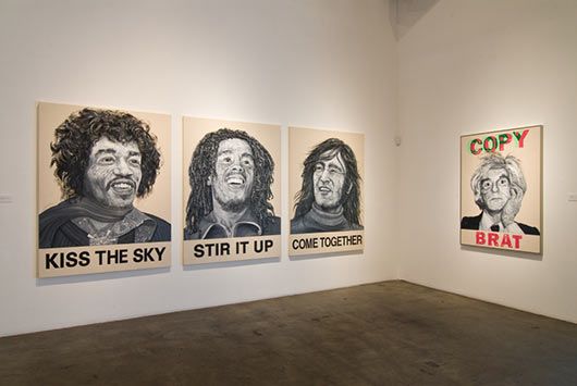 A room with a lot of paintings on the wall including one that says kiss the sky