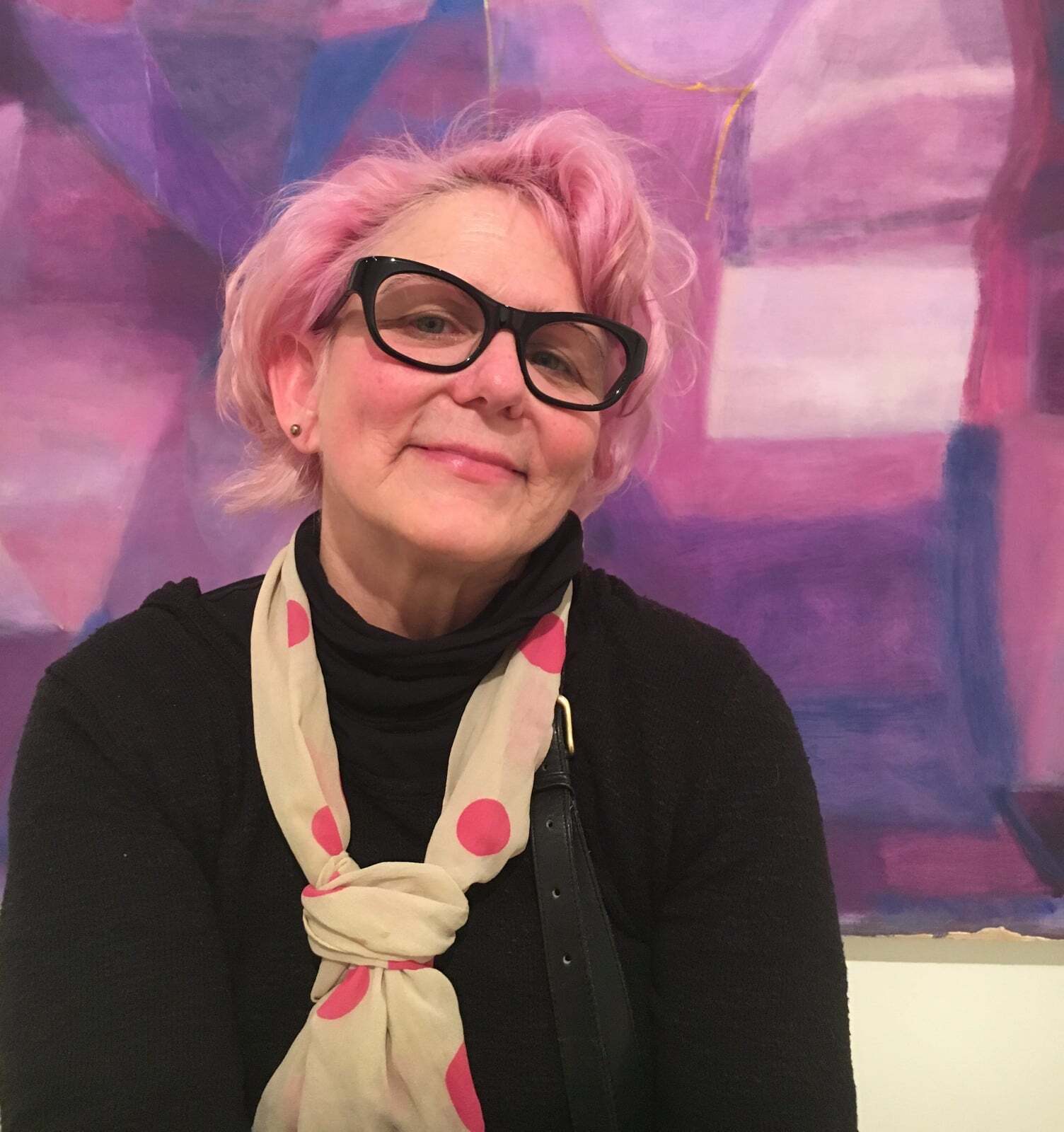 A woman with pink hair wearing glasses and a scarf