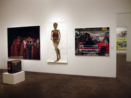 Three paintings are hanging on a wall in a museum