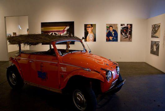 A red car is parked in a room with pictures on the wall