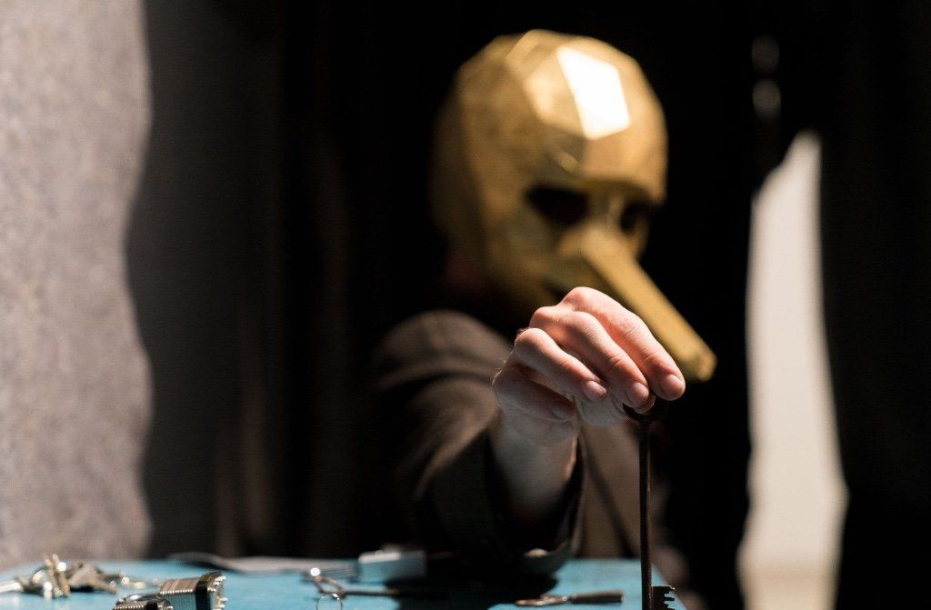 A person wearing a mask is sitting at a table with handcuffs.