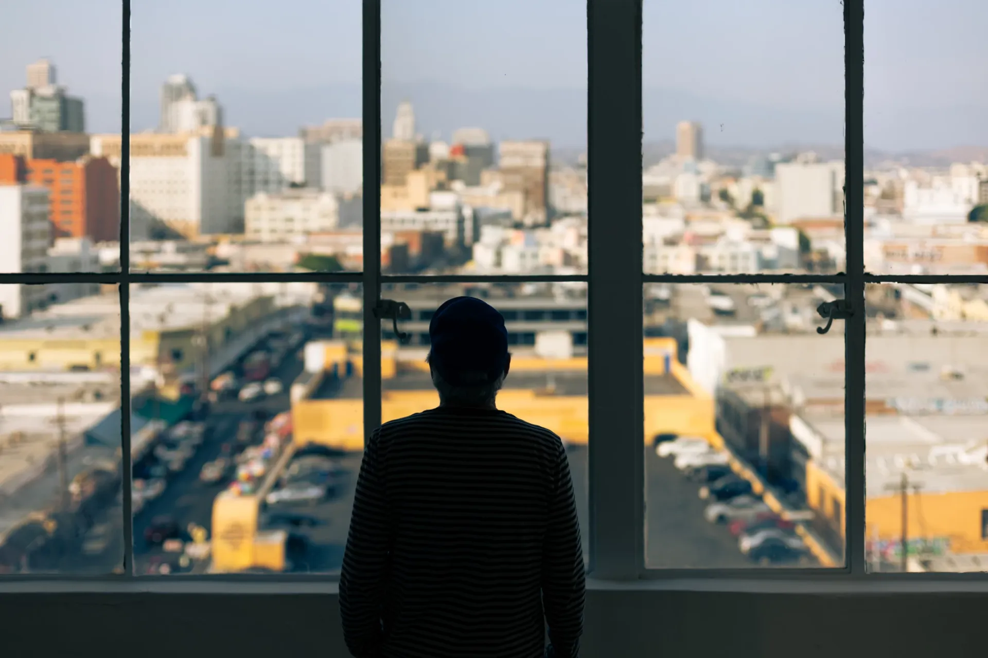 A man is standing in front of a window looking out at a city.