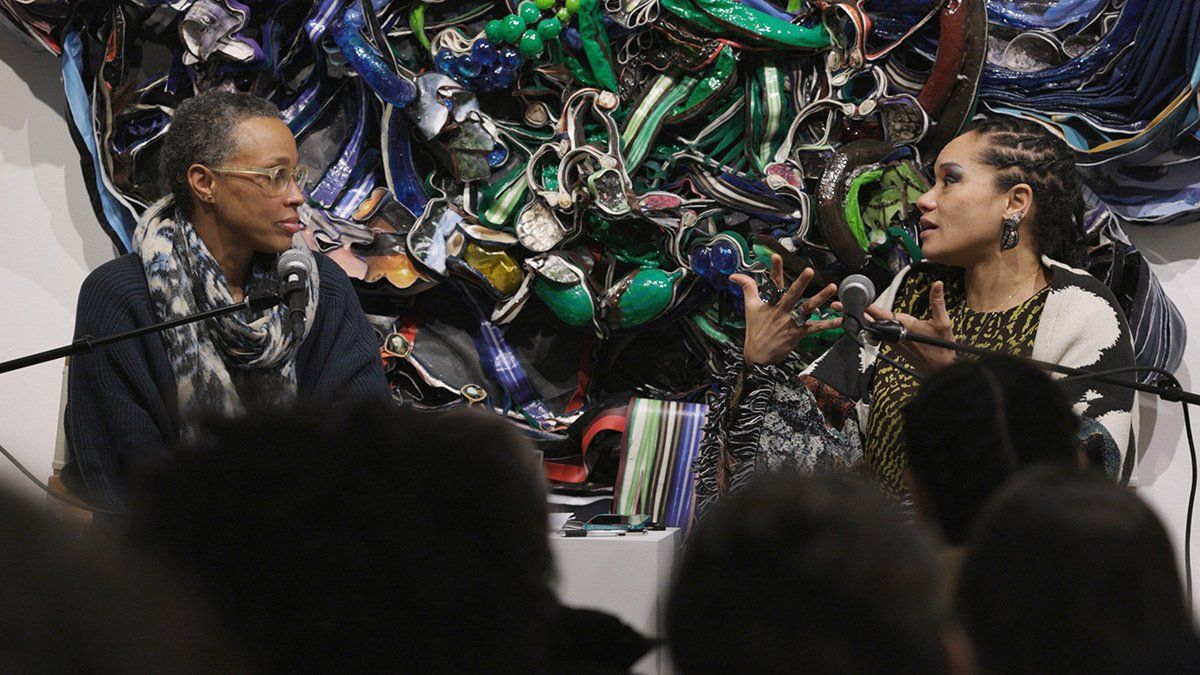 A man and a woman are talking in front of a microphone in front of a painting.
