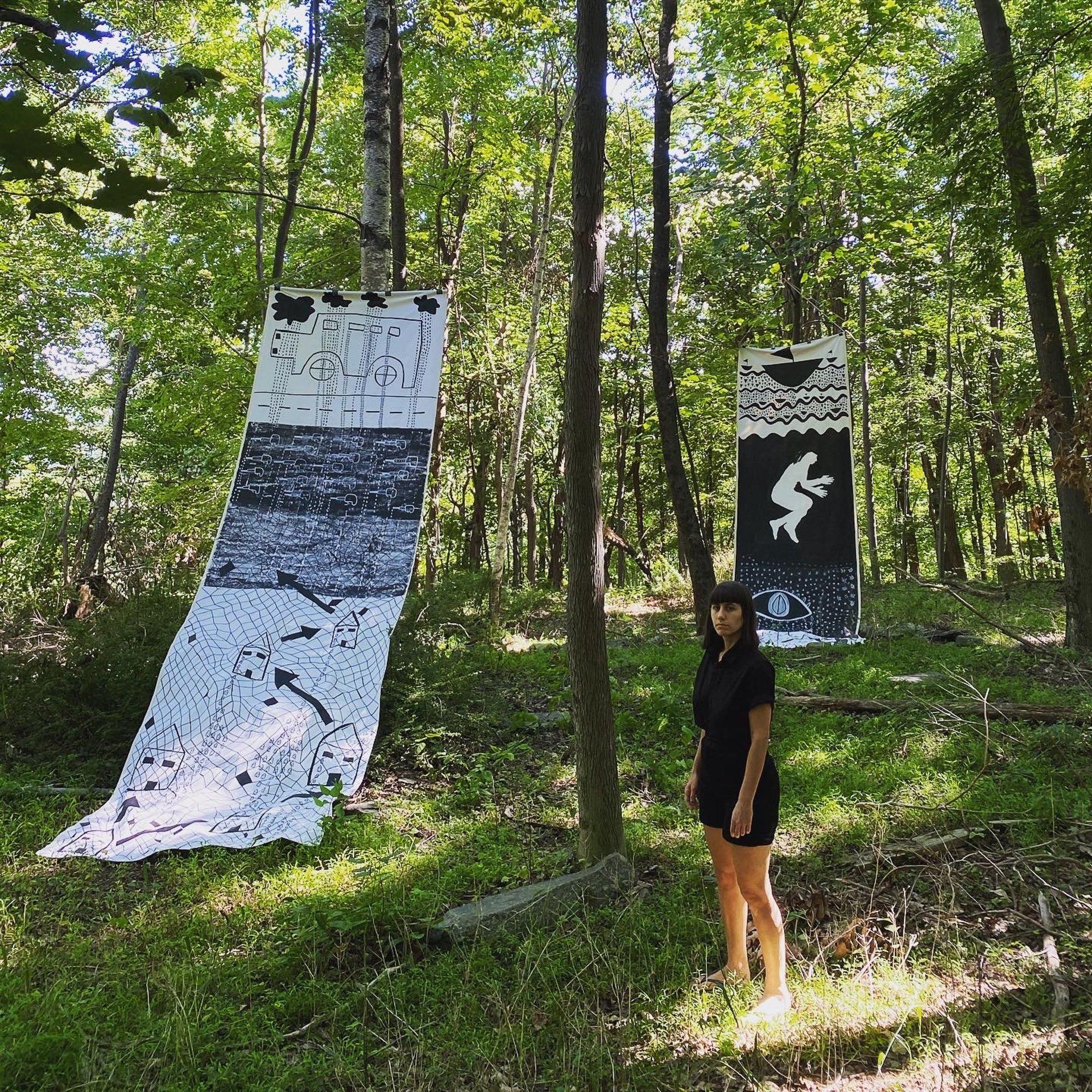 A woman is standing in the woods next to a large painting