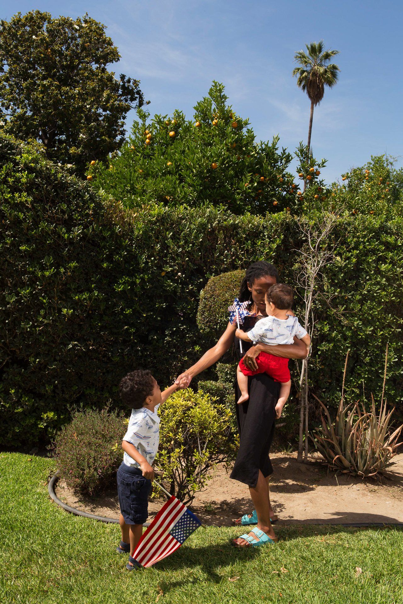 A woman is holding two children in her arms in a park.